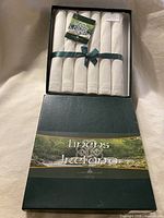 Box opened showing six rolled ivory linen napkins tied with green ribbon
