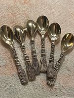All six spoons laid out showing fronts and decorative handles