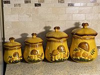Front view of four yellow glazed ceramic canisters with lids showing mushroom motif