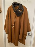 Full front view of rust brown wool cape with dark brown leather collar and buttons