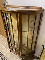 Full view of curved glass curio cabinet showing door, shelves, feet