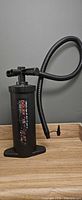 Black manual hand pump with hose on wooden surface