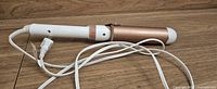 Side view of curling iron showing rose gold barrel, white handle and attached cord