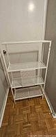 Full view of white metal mesh shelving unit showing three shelves and top frame shelf