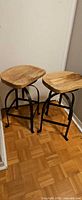 Two adjustable industrial stools with wood seats and metal frames visible