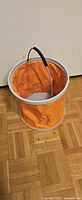 Bucket fully expanded showing orange body, gray rim, metal handle with foam grip