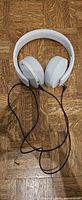 Over-ear white PlayStation gaming headset with attached black audio cable, top view on wood floor