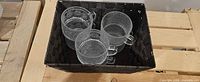 Four of the six clear pressed glass mugs visible in a basket