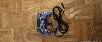 Blue camo Sony DualShock 4 controller with USB charging cable on wood floor