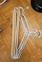 Five white metal and natural wood open-bar hangers stacked on floor