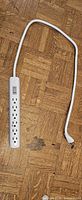 Full view of white 6-outlet power bar with cord and plug displayed on wood floor