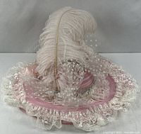 Side view of pink fascinator hat showing lace ruffle, polka dot tulle bow, rhinestone band and large ostrich feather