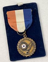 Front view of medal on ribbon showing emblem and wreath