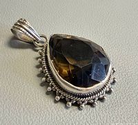 Front view of sterling silver pendant with faceted teardrop smoky quartz and ornate border