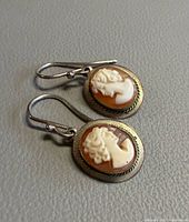 Pair of cameo drop earrings on grey surface, showing front and ear wires