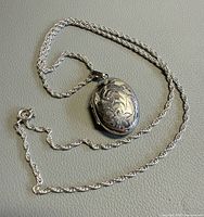Necklace laid flat showing entire rope chain and oval engraved locket