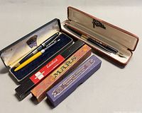 Overall lot showing thermometer box, two pen cases open with pens, two additional cardboard boxes