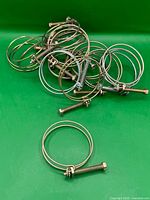 Pile of sixteen metal double wire hose clamps on green background