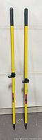 Two identical yellow broom handles standing upright