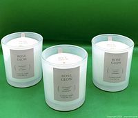Front view of three Rose Glow candles showing labels and wicks