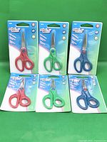 Six sealed School Works kids scissors displayed on green background