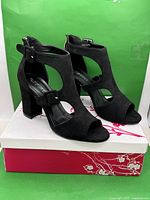 Pair of black strappy open-toe sandals on box, front and top view