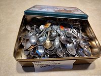 Tin box opened showing piled souvenir teaspoons
