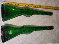 Two green rifle-shaped bottles beside tape for scale