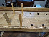 Workbench top showing dog holes, inlaid ruler, four wooden bench dogs inserted vertically, four black metal bench dogs on surface