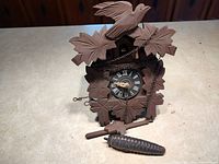 Front view of carved wood cuckoo clock with dial, chains, weight and pendulum visible