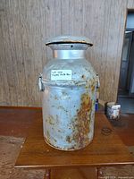 Full view of metal milk can showing lid, handles, rust patina, size context