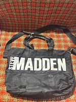 Front view of black Steve Madden bag showing logo and handles