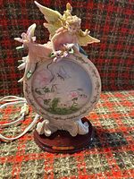 Front view of porcelain angel figurine with floral panel and wood base, showing overall design and power cord