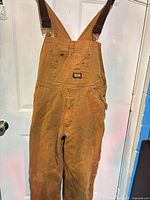 Full view of brown insulated bib overalls hanging