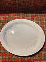 Front view of white oval platter showing embossed fruit and vine border