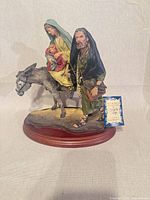 Front view of signed ceramic Holy Family on donkey figurine with wood base and tag