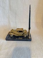 Side view showing brass car figurine, pen socket, and pen on marble base
