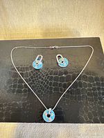 Necklace with donut pendant and both earrings displayed on black surface