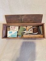 Open wooden box with assorted vintage office supply boxes and metal punch visible