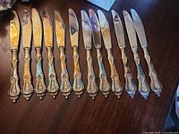 Top view of 12 ornate silver-plated knives laid out