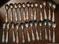Full set of 24 ornate silverplate dessert spoons laid out