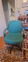 Front view of teal fabric desk chair showing seat, back, armrests and wheeled base