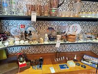 Wide shot of three-shelf unit showing figurines, glassware, dessert bowls, plates, metal miniatures