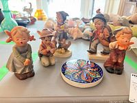 Five Hummel figurines and ceramic coaster overview