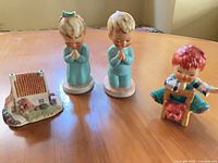 Group shot of four figurines: two praying children, seated boy with puppy, ceramic cottage