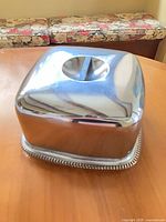 Chrome cake carrier on table, full view with cover on base