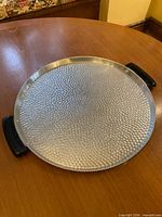 Top view of round hammered aluminum tray with black handles