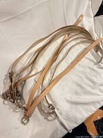 Ten light tan leather belts coiled together on white surface