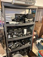 Four-shelf unit filled with black receipt printers, stacked silver Mac minis, cabling