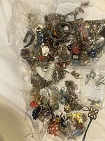 Overview of mixed costume jewelry piled on white surface, some in clear plastic bags